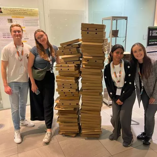 Four members of the Preston lab stand either side of two head high pizza box stacks at the end of the ECPP24 reception in September 2024